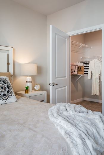 A bedroom with a bed, a nightstand with a clock, a lamp, and an open closet.